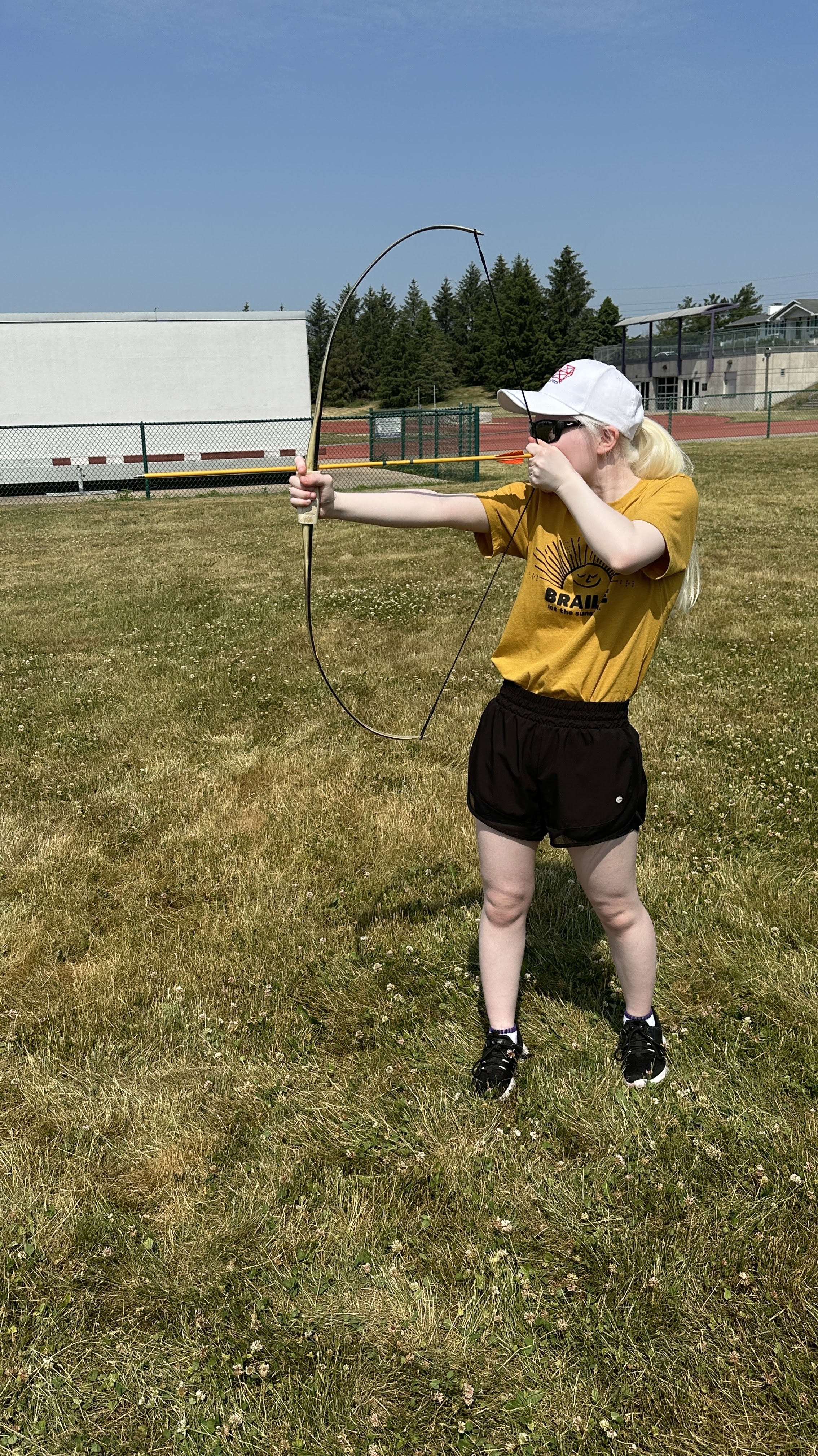 A picture of Leah standing in grass aiming an arrow in archery.