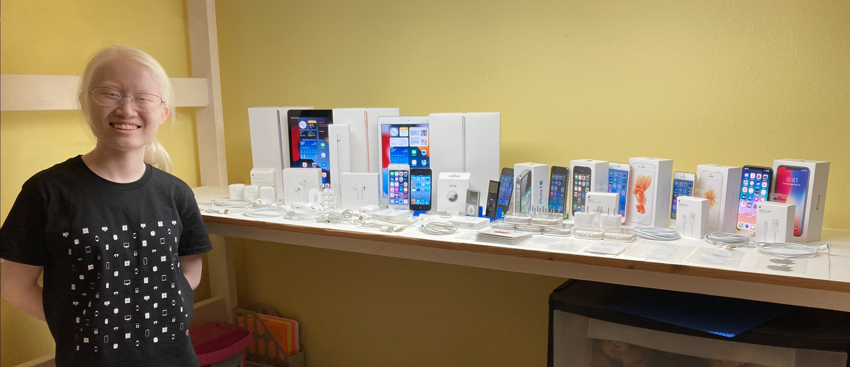Leah kneeling beside her collection of Apple products displayed on a desk behind and to the side of her.