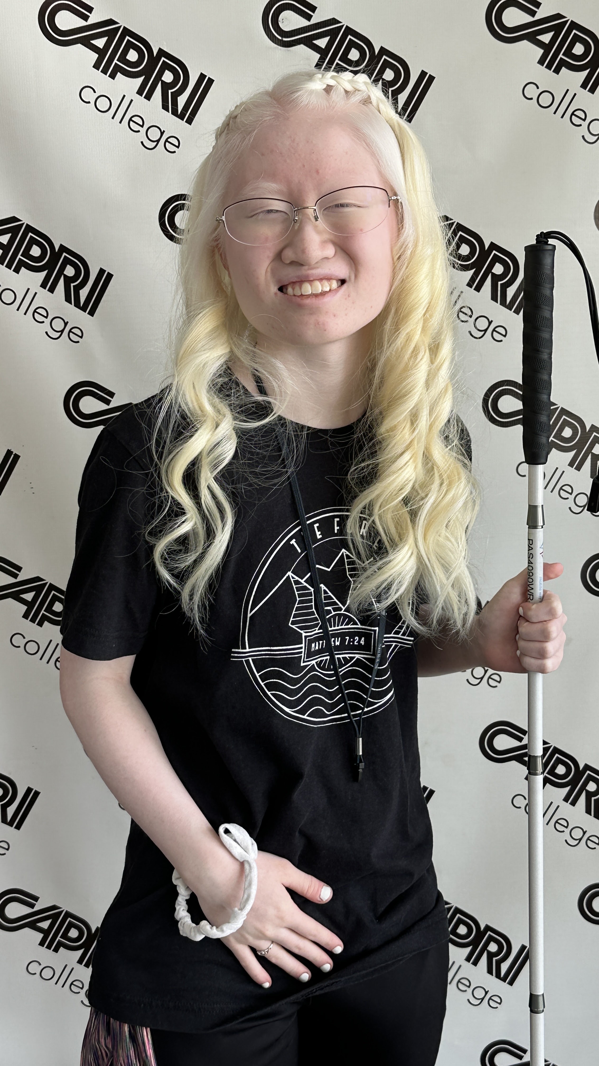 Leah posing with curled hair in front of the Capri College hair salon wall.